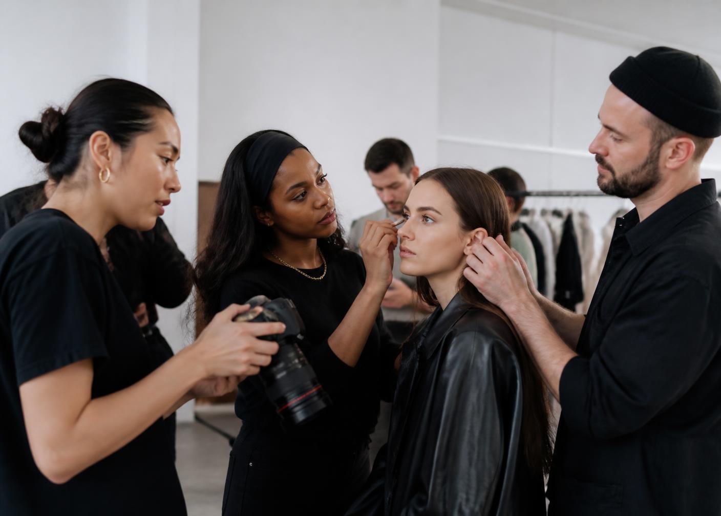 Creative production team including a photographer, makeup artist and stylist preparing a model backstage